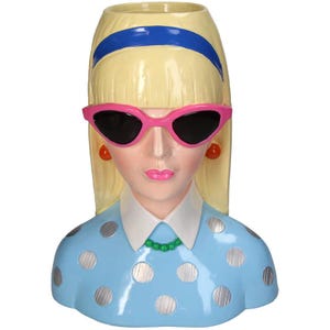 May include: A ceramic vase shaped like a woman's bust. The woman has blonde hair, pink sunglasses, and is wearing a blue dress with white polka dots.