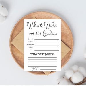May include: A white rectangular card with black text reading Wishes & Wisdom For The Graduate, featuring lines for Always, Never, Remember, Enjoy, Visit, and a section for a special message or wish, placed on a brown envelope and wooden plate.