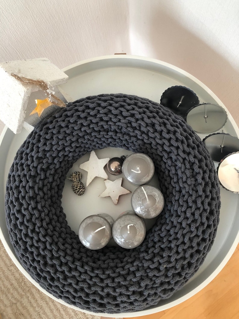 May include: A gray knitted wreath with four gray candles and white stars on a white tray.