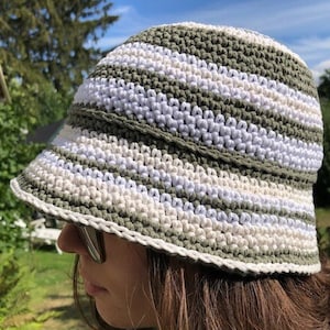 Puede incluir: Un sombrero de cubo de crochet a rayas verdes y blancas. El sombrero tiene un ala ancha y est&aacute; hecho con un patr&oacute;n de punto simple.