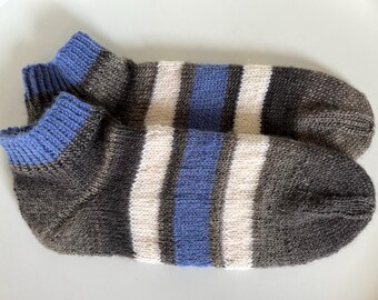 Puede incluir: Un par de calcetines de punto con un diseño de rayas. Los calcetines presentan bandas azules, blancas y grises. Los puños son azules. Los calcetines están hechos de un material suave y texturizado.