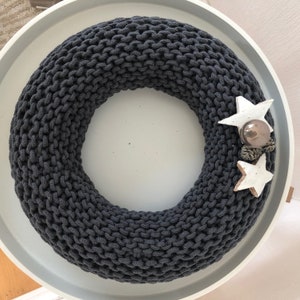 May include: A dark gray knitted wreath with two white star ornaments and a brown pine cone ornament.