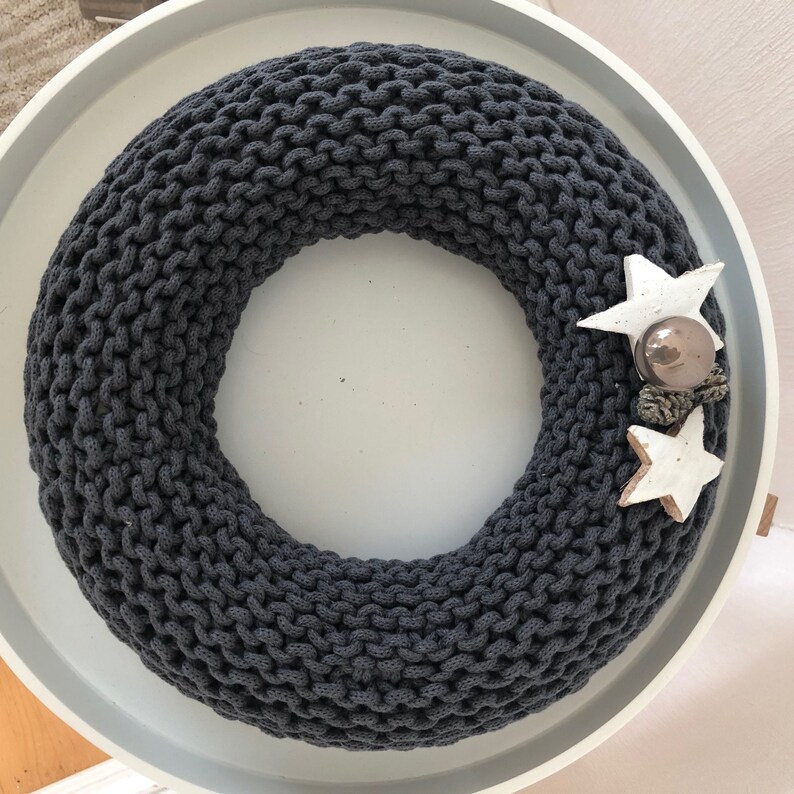 May include: A dark gray knitted wreath with two white star ornaments and a brown pine cone ornament.