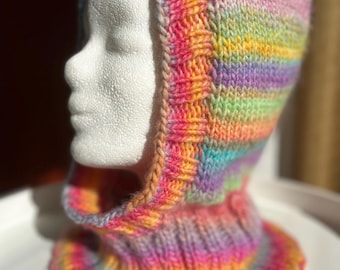 Puede incluir: Un gorro de punto colorido con capucha y cuello ancho. El gorro está hecho con un arcoíris de colores, incluyendo rosa, amarillo, verde y azul.
