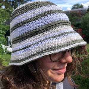 Puede incluir: Un sombrero de cubo de crochet a rayas verdes y blancas. El sombrero tiene un ala ancha y est&aacute; hecho con un hilo suave y texturizado.