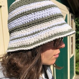 Puede incluir: Un sombrero de cubo de crochet a rayas verdes y blancas. El sombrero est&aacute; hecho con un hilo suave y texturizado y tiene un ala ancha.