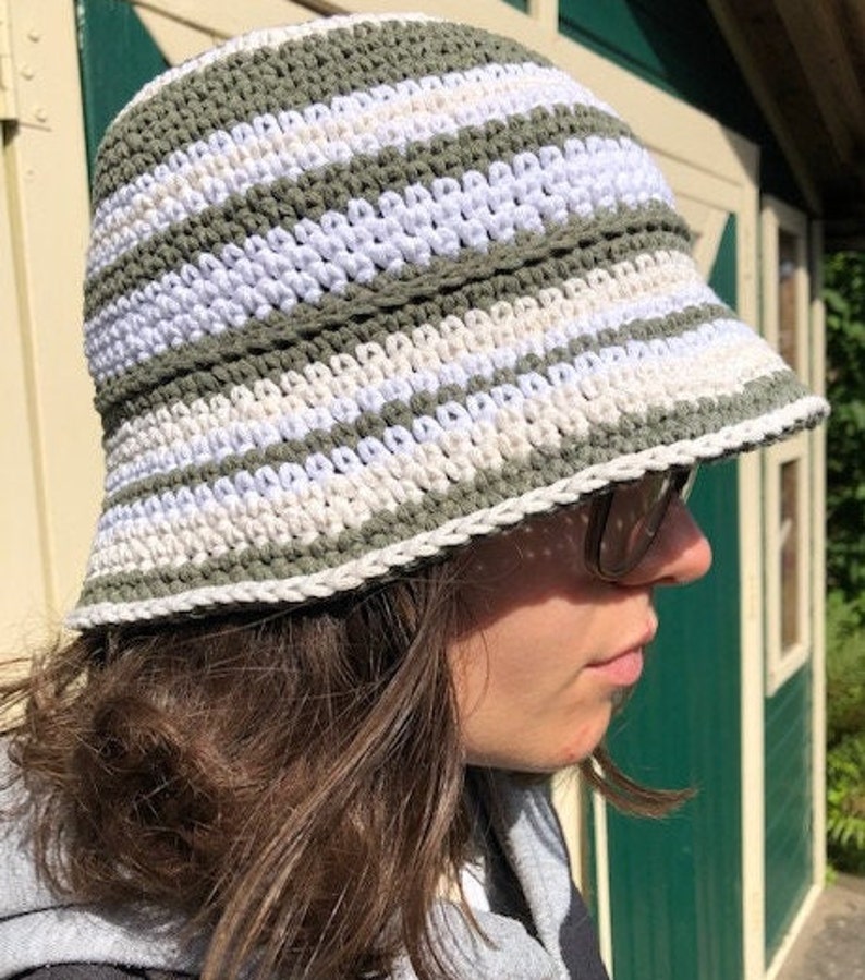 Puede incluir: Un sombrero de cubo de crochet a rayas verdes y blancas. El sombrero est&aacute; hecho con un hilo suave y texturizado y tiene un ala ancha.