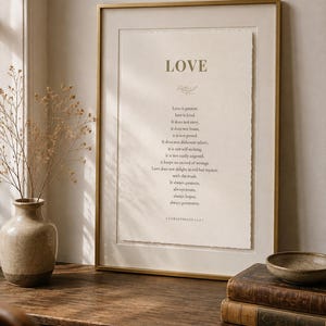 May include: A framed wall art print featuring the text LOVE and the 1 Corinthians 13:4-7 Bible verse printed in dark ink on off-white paper with a deckled edge. The print is housed in a thin gold metal frame with a wide off-white matting border.