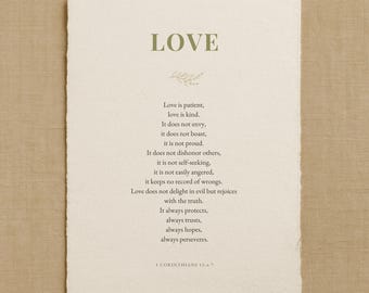 May include: A rectangular off-white paper print with deckled edges featuring the word LOVE in olive green at the top, a small leaf illustration, and the text of 1 Corinthians 13:4-7 in dark gray, ending with the citation 1 CORINTHIANS 13:4-7.