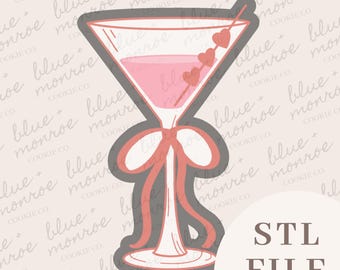 May include: A pink cocktail cookie cutter with a bow detail. The martini glass has a pink liquid and a skewer with three hearts. The words "STL FILE" are in the bottom right corner. The background has a repeating pattern of the words "blue + monroe cookie co."