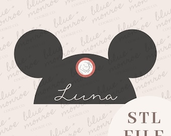 May include: A black cookie cutter in the shape of a mouse head with the name "Luna" in cursive. A small circular design with a flower is above the name. The text "STL FILE" is in the lower right corner.