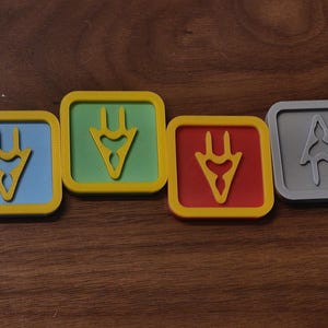 May include: Four square coasters with a yellow border. The coasters have different coloured centres: blue, green, red, and grey. Each coaster features a stylized yellow symbol in the centre.