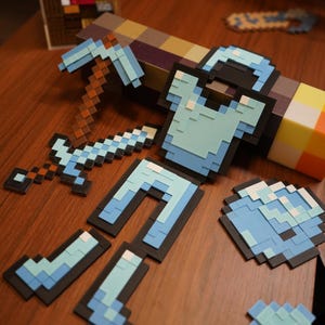May include: A collection of pixelated Minecraft-style items, including armour, tools, and weapons. The set features blue, brown, and black elements, such as a chest plate, leggings, helmet, pickaxe, sword, and axe. Items are on a wooden surface.