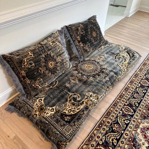 May include: A gray and gold patterned floor cushion with fringe. The cushion is made of a soft, plush fabric and is perfect for lounging or meditation.