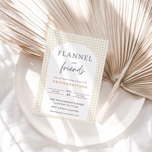 May include: A beige and white gingham patterned invitation card with the text "FLANNEL and friends" in black and gold lettering. The invitation is for a Friendsgiving event on Saturday, November 21st at 4 o'clock. The event is being held at The Williamson's Home, 123 Any Street, City, ST 12345. RSVP to Kate at 123-456-7890. The invitation requests guests to bring their favorite side dish to share.