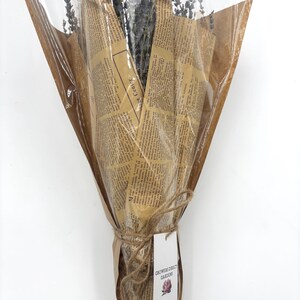 May include: A bouquet of dried lavender wrapped in brown paper with a newspaper print design. The bouquet is tied with twine and has a tag that reads "Growers Direct Gardens".