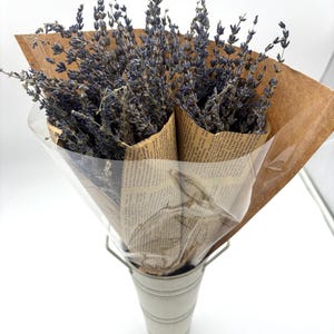 May include: A bouquet of dried lavender flowers wrapped in brown paper and tied with twine. The bouquet is in a white metal vase.