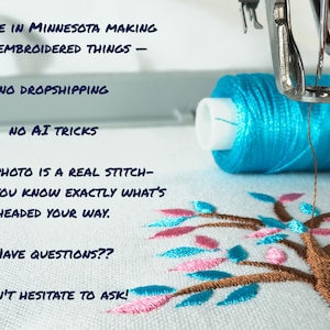 May include: An embroidery machine needle positioned over white fabric with a brown, blue, and pink tree design. Text reads: JUST ME IN MINNESOTA MAKING COOL EMBROIDERED THINGS - NO DROPSHIPPING NO AI TRICKS EVERY PHOTO IS A REAL STITCH-OUT, SO YOU KNOW EXACTLY WHAT'S HEADED YOUR WAY. HAVE QUESTIONS?? DON'T HESITATE TO ASK!