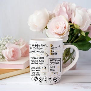 May include: White ceramic mug with black and gold lettering. The mug has a birthday theme with the text "It's probably time to start lying about your age" and "So happy I'm thirty". The mug also has a birthday checklist with the text "Older" and "Wiser".