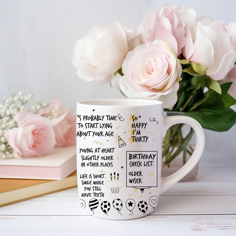 May include: White ceramic mug with black and gold lettering. The mug has a birthday theme with the text "It's probably time to start lying about your age" and "So happy I'm thirty". The mug also has a birthday checklist with the text "Older" and "Wiser".