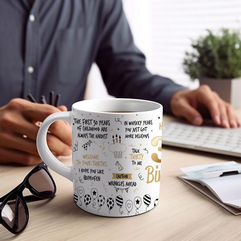 May include: White ceramic mug with a gold design. The mug features a humorous message about turning 30, including the text "The first 30 years of childhood are always the hardest", "Welcome to your thirties", "I hope you like ibuprofen", "In whiskey years you just got more delicious", "Talk thirty to me", and "Caution wrinkles ahead".