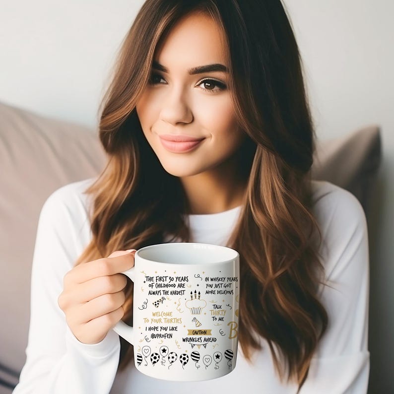 May include: White ceramic mug with a gold design and text that reads "The first 30 years of childhood are always the hardest. Welcome to your thirties. I hope you like ibuprofen. In whiskey years you just got more delicious. Talk thirty to me. Caution wrinkles ahead."