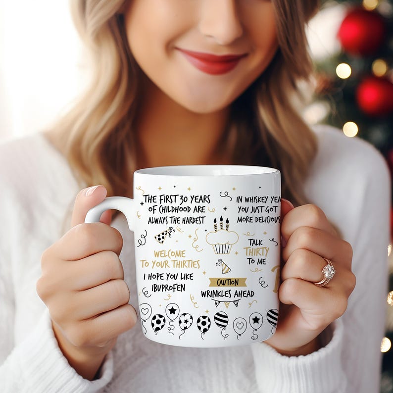 May include: White ceramic mug with black and gold text and illustrations. The text reads "The first 30 years of childhood are always the hardest. Welcome to your thirties. I hope you like ibuprofen. In whiskey years you just got more delicious. Talk thirty to me. Caution wrinkles ahead."