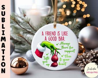 Puede incluir: Un adorno navideño redondo blanco con una mano verde del Grinch sosteniendo un sujetador rojo con el texto "Un amigo es como un buen sujetador: Siempre ahí para el apoyo, Cerca de tu corazón." El adorno está rodeado de decoraciones navideñas.