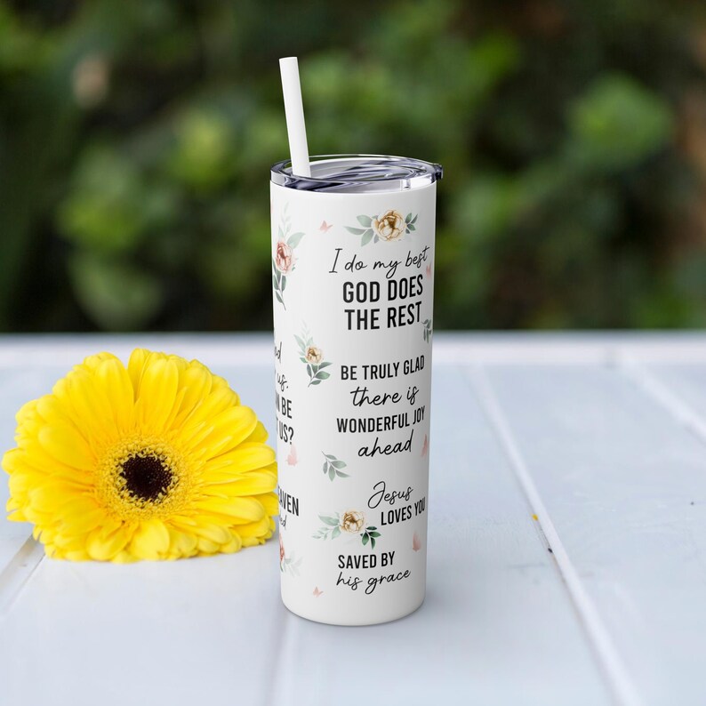 May include: White stainless steel tumbler with a floral design and inspirational quotes. The quotes include "I do my best, God does the rest", "Be truly glad, there is wonderful joy ahead", "Jesus loves you", and "Saved by his grace".