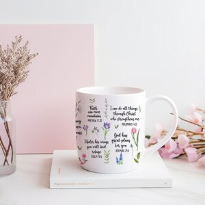 May include: White ceramic mug with inspirational quotes and floral designs. The quotes include "Faith can move mountains", "I can do all things through Christ who strengthens me", "God has great plans for you", and "Under his wings you will find refuge".