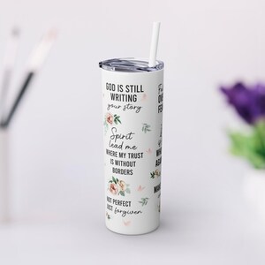 May include: White tumbler with a floral design and the text "God is still writing your story. Spirit lead me where my trust is without borders. Not perfect just forgiven."