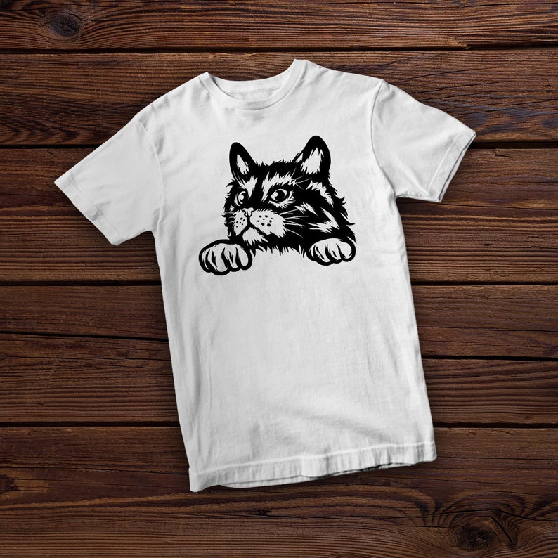 May include: White t-shirt with a black and white illustration of a cat peeking over the edge of the shirt.