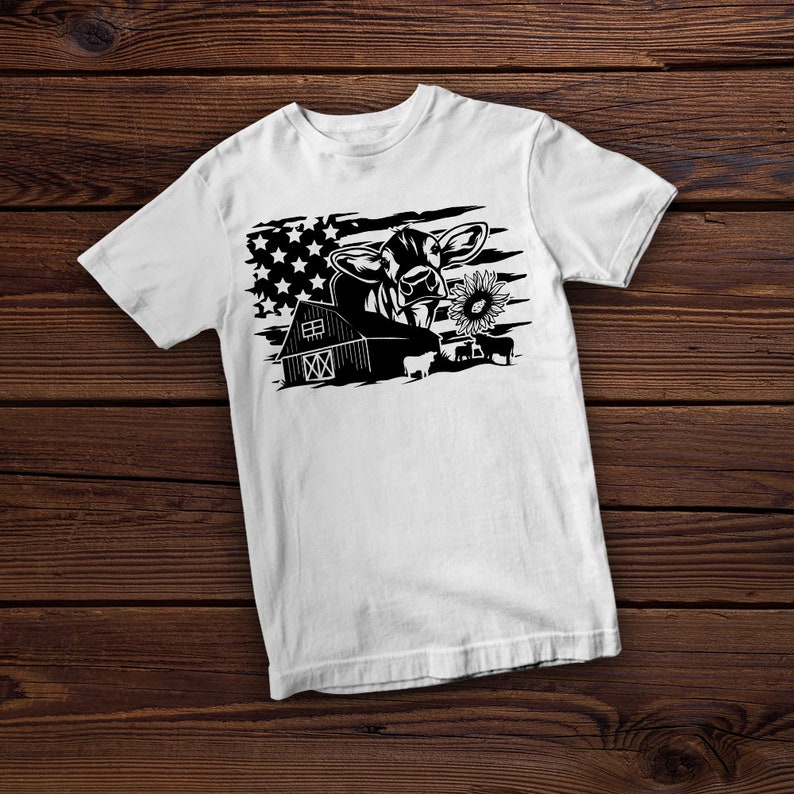 May include: White t-shirt with a black and white graphic of a cow with a sunflower in its mouth, a barn, and an American flag in the background.