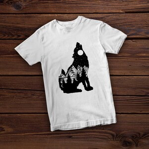 May include: White t-shirt with a black silhouette of a wolf howling at the moon. The wolf's silhouette is filled with a mountain landscape and stars.