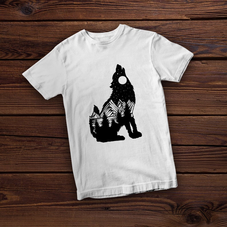 May include: White t-shirt with a black silhouette of a wolf howling at the moon. The wolf's silhouette is filled with a mountain landscape and stars.