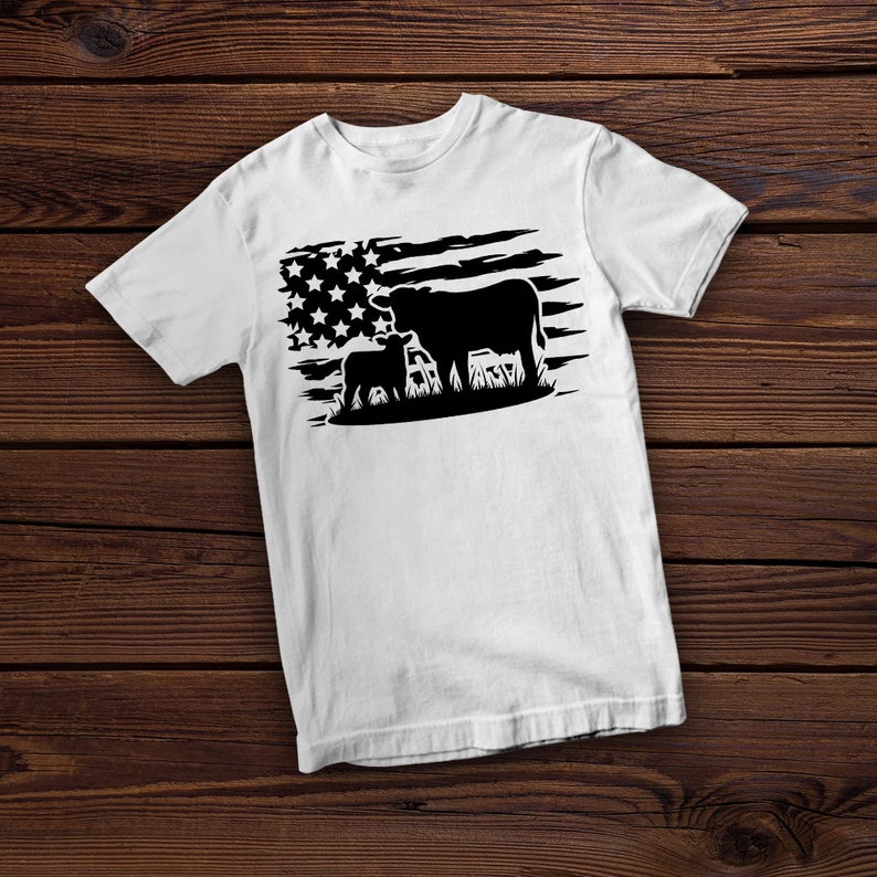 May include: White t-shirt with a black silhouette of a cow and calf standing in front of a distressed American flag.