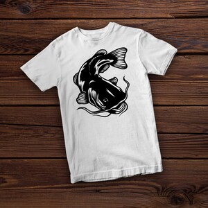 May include: White t-shirt with a black silhouette of a catfish. The catfish is facing the left side of the image and has its mouth open.
