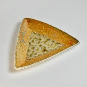 May include: A triangular ceramic dish with a textured surface. The dish features a blend of orange, yellow, and green hues. The edges have a white border. The interior has a patterned design.
