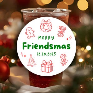 Könnte beinhalten: Ein runder weißer Aufkleber mit dem grünen Text Merry Friendsmas und dem Datum 12.20.2025. Das Design enthält rote Strichzeichnungen eines Lebkuchenmanns, eines Kranzes, eines Kelchs, eines Weihnachtsbaums, eines Geschenks und einer Zuckerstange.