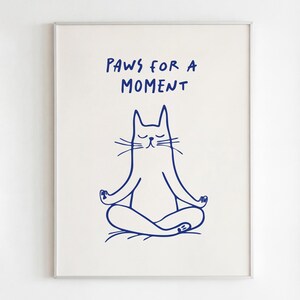 以下が含まれることがあります： ヨガのポーズをとる猫の青い線画が描かれた額入りのプリント。テキスト「PAWS FOR A MOMENT」が猫の上にあります。猫は目を閉じて、手を合わせて瞑想しています。