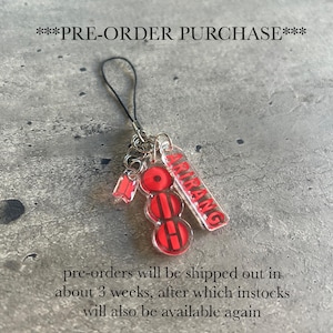 Może przedstawiać: Przezroczysty akrylowy urok z czerwonymi akcentami i słowem "ARIRANG" w kolorze czerwonym. Urok zawiera czerwono-czarny wzór i mały czerwony urok. Tekst "***PRE-ORDER PURCHASE***" znajduje się na górze.