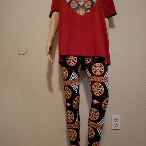 May include: A red t-shirt with a black heart-shaped design featuring a geometric pattern. The t-shirt is paired with black leggings with a geometric pattern in red, yellow, and white.