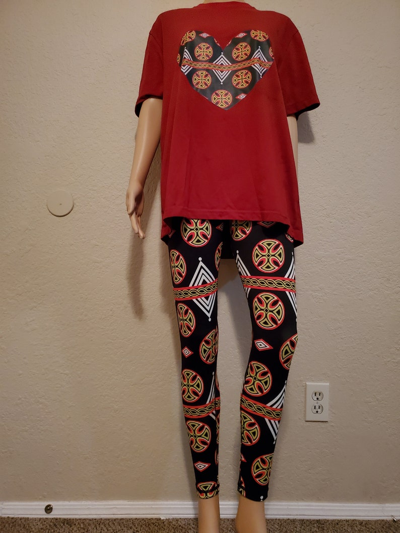 May include: A red t-shirt with a black heart-shaped design featuring a geometric pattern. The t-shirt is paired with black leggings with a geometric pattern in red, yellow, and white.