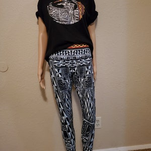 May include: Black and white leggings with a geometric pattern. The leggings have a black waistband with a red and yellow geometric pattern. The leggings are paired with a black t-shirt with a white and orange geometric pattern.