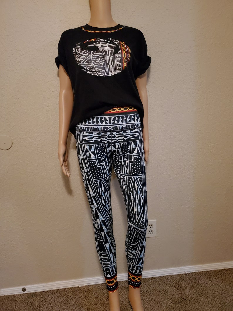 May include: Black and white leggings with a geometric pattern. The leggings have a black waistband with a red and yellow geometric pattern. The leggings are paired with a black t-shirt with a white and orange geometric pattern.