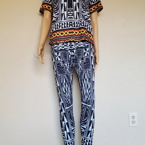 May include: A black and white patterned two-piece outfit with a short-sleeved top and leggings. The top has a red, yellow, and black trim. The leggings have a yellow and red trim at the bottom.