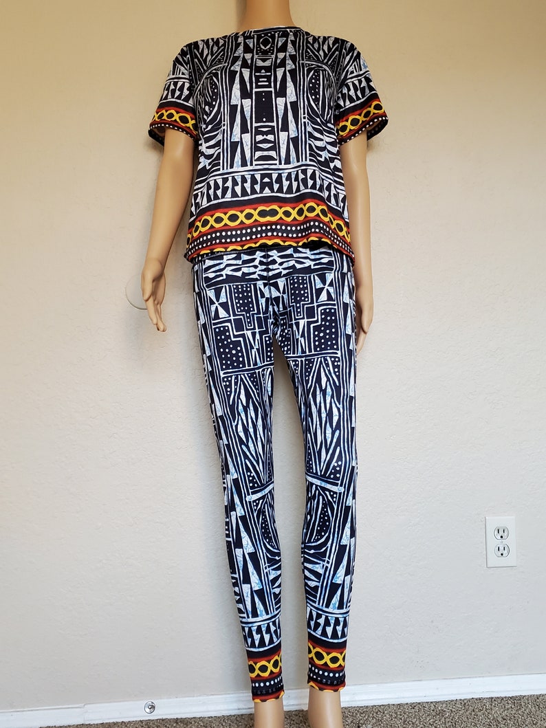 May include: A black and white patterned two-piece outfit with a short-sleeved top and leggings. The top has a red, yellow, and black trim. The leggings have a yellow and red trim at the bottom.