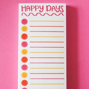 May include: A white notepad with the words "HAPPY DAYS" in pink lettering at the top. The notepad has a line for each day of the month with a smiley face icon next to each line. The smiley faces are in alternating colors of pink, orange, and yellow.