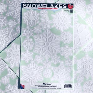 May include: White snowflake window clings in various sizes and designs are displayed on a light green background. The package reads "Snowflakes Reusable Window Clings" with the number "120" in the corner. The clings are perfect for winter holiday decorations.