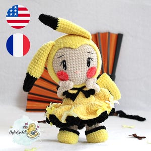 Könnte beinhalten: Ein gehäkeltes Pikachu Plüschtier, das ein gelbes Kleid mit schwarzen Akzenten und einer schwarzen Schleife trägt. Das Spielzeug hat ein hellbraunes Gesicht mit roten Wangen und großen schwarzen Augen.